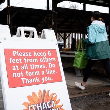 Person walking into the Ithaca Farmers Market next to a sign with instructions on social distancing